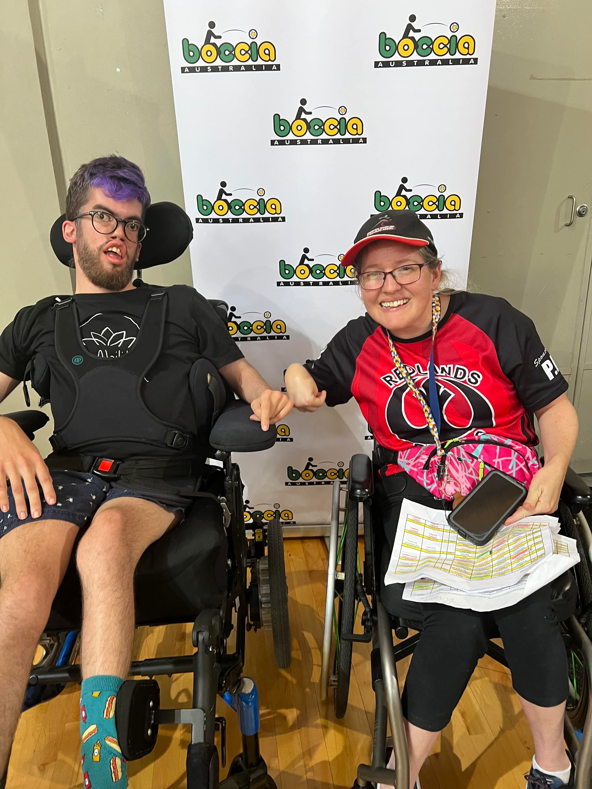 Two teammates fist-bumping in front of a Boccia Australia backdrop